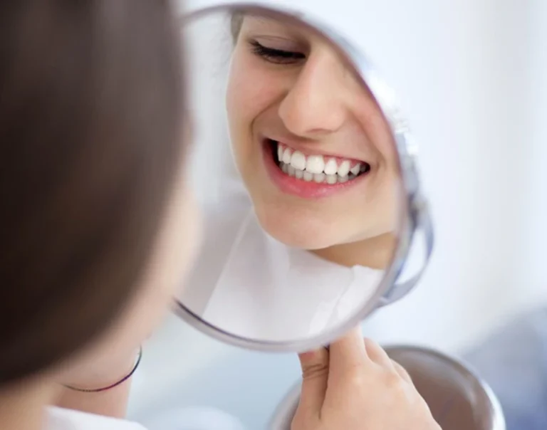 Patiente souriante découvrant ses dents blanchies dans un miroir