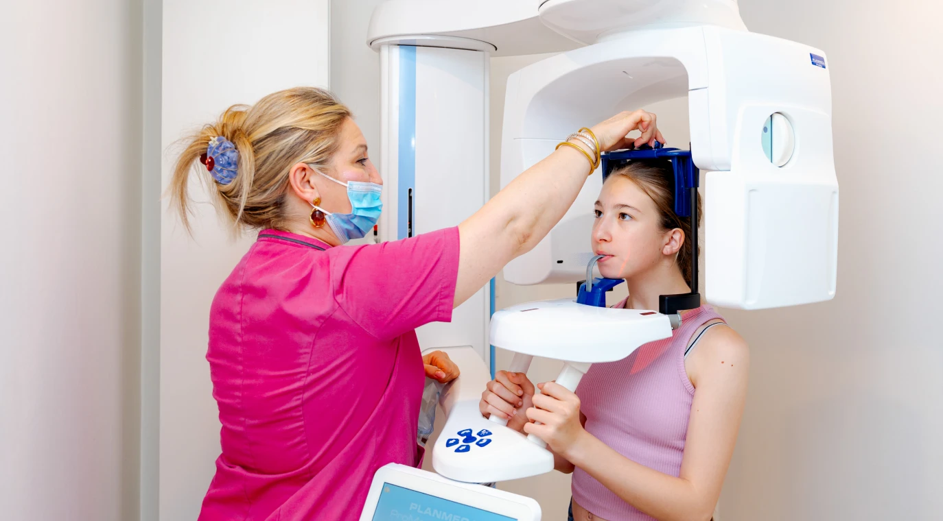 Assistante positionnant une jeune patiente devant l’appareil de radiographie panoramique