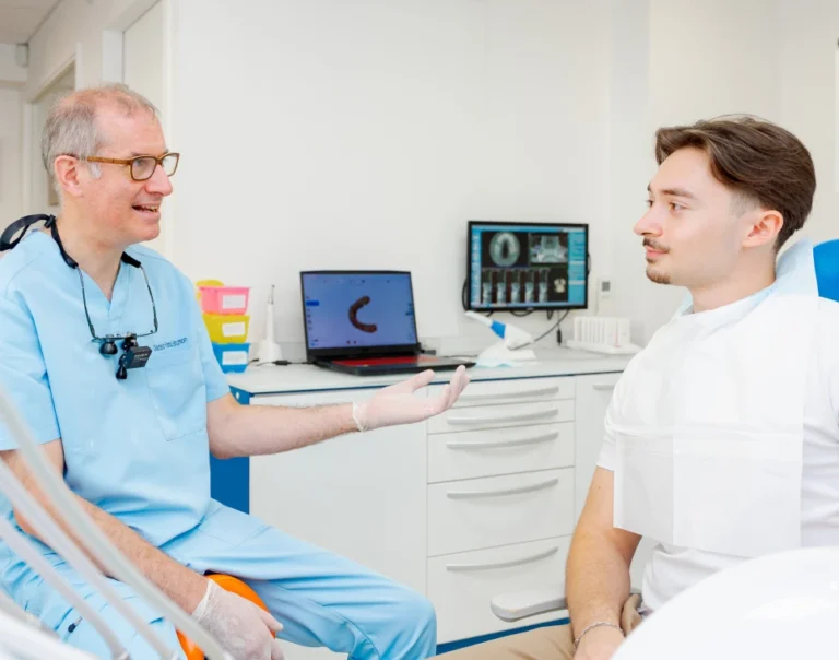 Dentiste échangeant avec un jeune patient au fauteuil, radiographie à l’écran