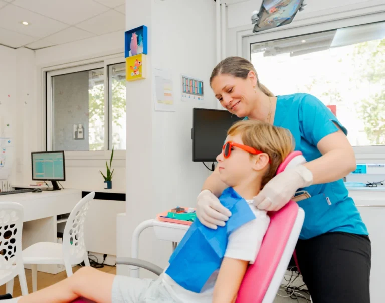 Enfant installé au fauteuil avec lunettes de protection, rassuré par la dentiste